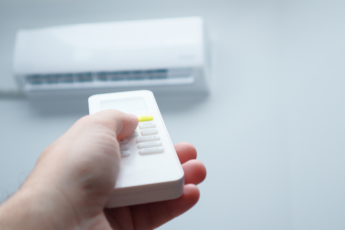 Air conditioner inside the room with man operating remote controller. Air conditioner with remote controller